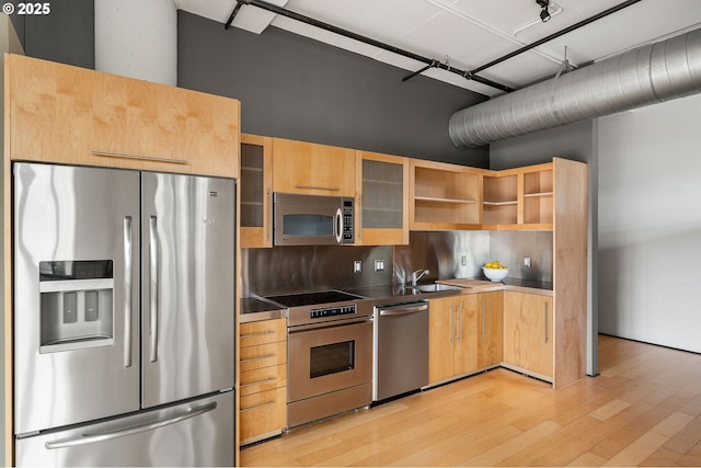 kitchen with stainless steel appliances, light wood-style flooring, a sink, dark countertops, and glass insert cabinets