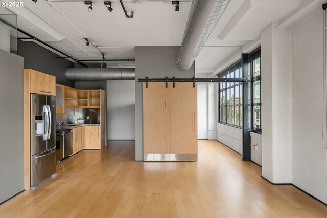 kitchen featuring stainless steel fridge, light wood-style floors, open shelves, light brown cabinets, and a barn door