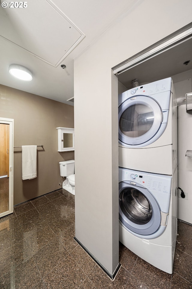 laundry room featuring stacked washer / drying machine, granite tiled floors, and attic access