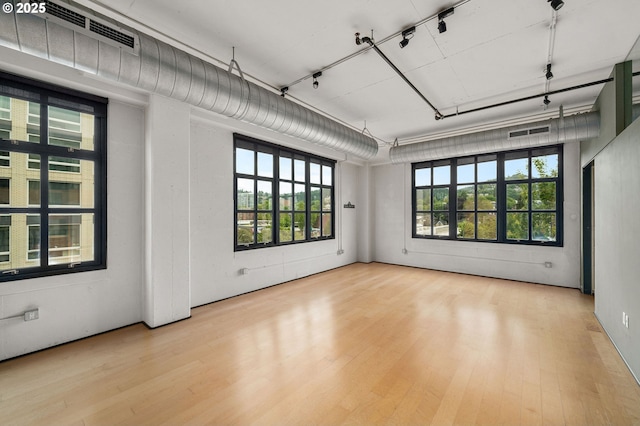 empty room with wood finished floors, plenty of natural light, and rail lighting