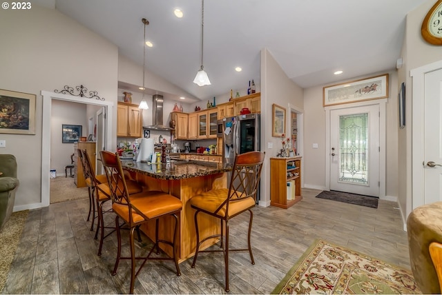 48482 E Meadow Way, Oakridge, OR 97463 - kitchen with wall chimney range hood, a breakfast bar, glass insert cabinets, light wood finished floors, and dark stone counters