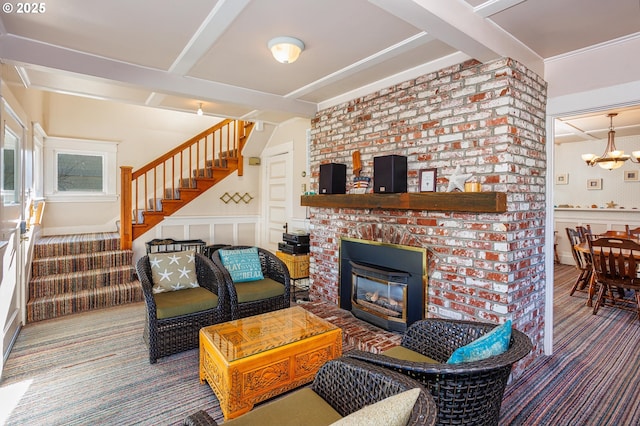 living room with beamed ceiling, a brick fireplace, carpet flooring, and a notable chandelier