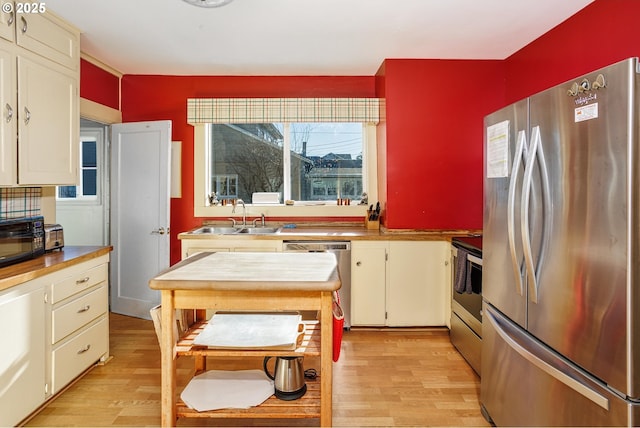 kitchen with sink, cream cabinets, light wood-type flooring, and appliances with stainless steel finishes