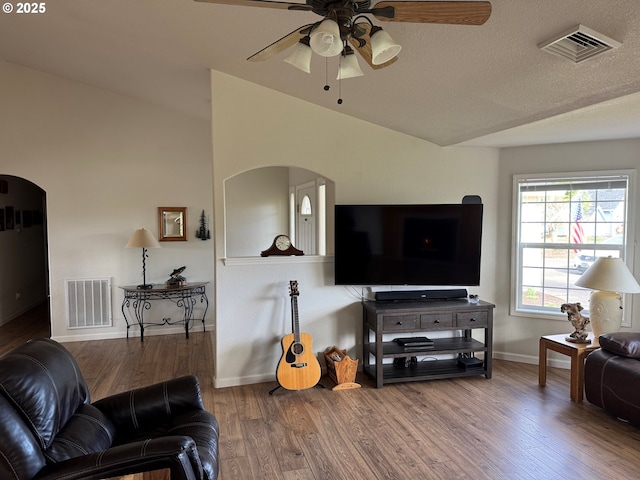 living room featuring vaulted ceiling, wood finished floors, visible vents, and arched walkways