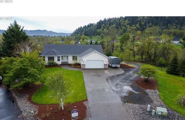 ranch-style home featuring driveway, a view of trees, a mountain view, a front yard, and a garage