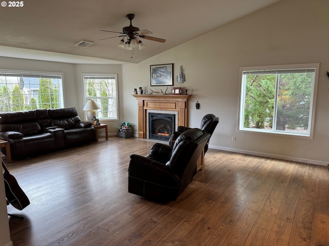 living area with baseboards, visible vents, lofted ceiling, a fireplace with flush hearth, and wood-type flooring