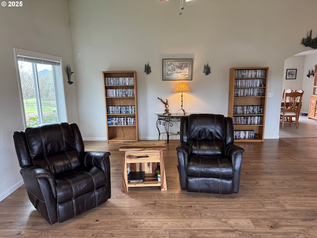 sitting room with arched walkways, wood finished floors, and a towering ceiling