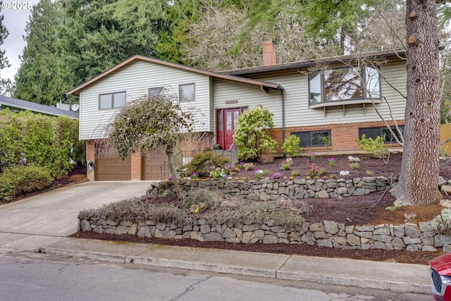 raised ranch with concrete driveway, a garage, brick siding, and a chimney