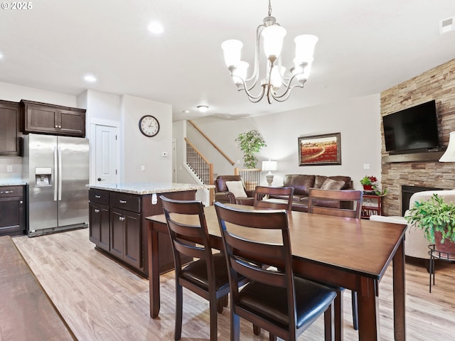 dining space featuring light wood-type flooring, a chandelier, and a fireplace