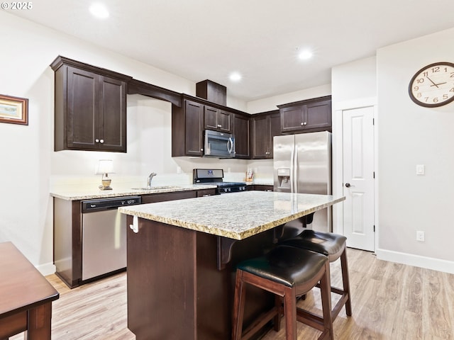 kitchen with a kitchen island, appliances with stainless steel finishes, sink, dark brown cabinets, and light hardwood / wood-style flooring