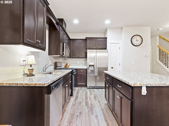 kitchen featuring sink, appliances with stainless steel finishes, dark brown cabinetry, light stone counters, and light wood-type flooring