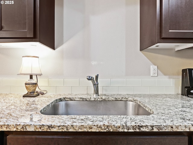 kitchen with sink, light stone counters, and dark brown cabinetry