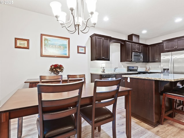 kitchen with dark brown cabinets, hanging light fixtures, appliances with stainless steel finishes, a kitchen island, and light stone countertops