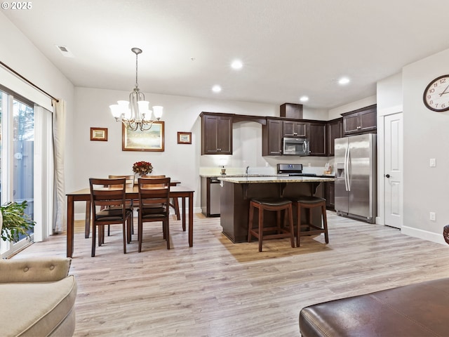 kitchen with appliances with stainless steel finishes, hanging light fixtures, dark brown cabinets, and light hardwood / wood-style flooring