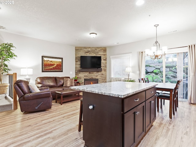 kitchen featuring dark brown cabinetry, decorative light fixtures, a center island, a textured ceiling, and light wood-type flooring