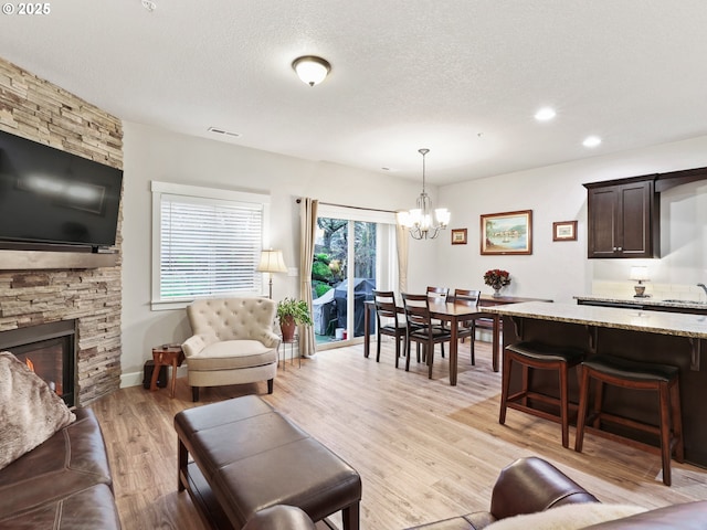 living room with a stone fireplace, an inviting chandelier, a textured ceiling, and light hardwood / wood-style floors