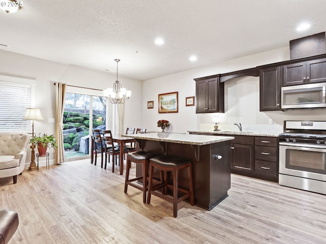 kitchen featuring dark brown cabinetry, sink, light stone counters, light wood-type flooring, and appliances with stainless steel finishes