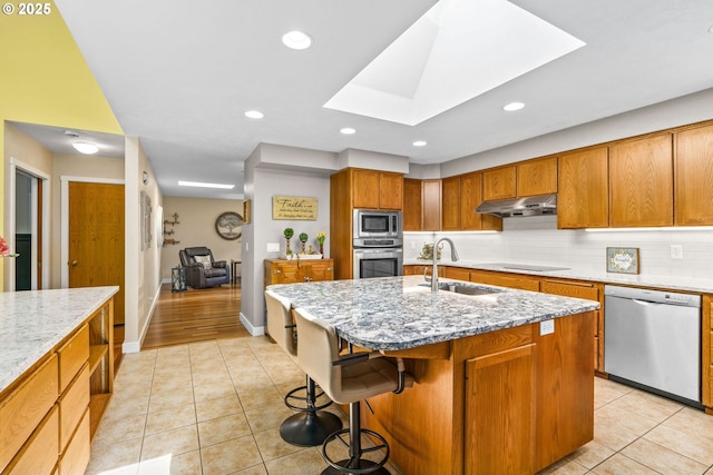 kitchen with under cabinet range hood, light stone counters, a sink, light tile patterned floors, and stainless steel appliances