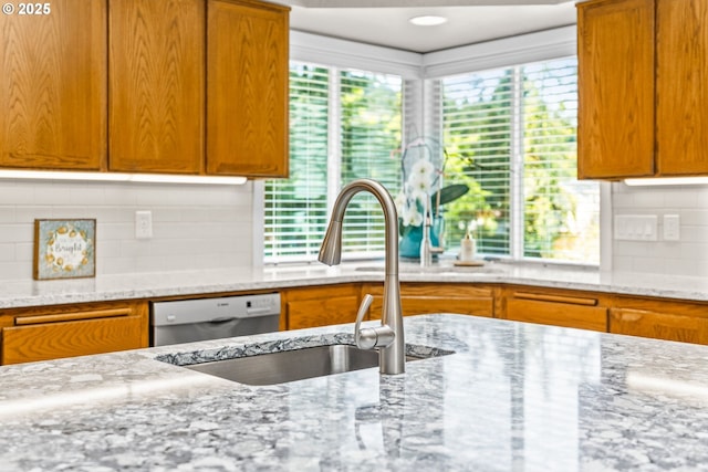 kitchen with stainless steel dishwasher, light stone counters, decorative backsplash, and a sink