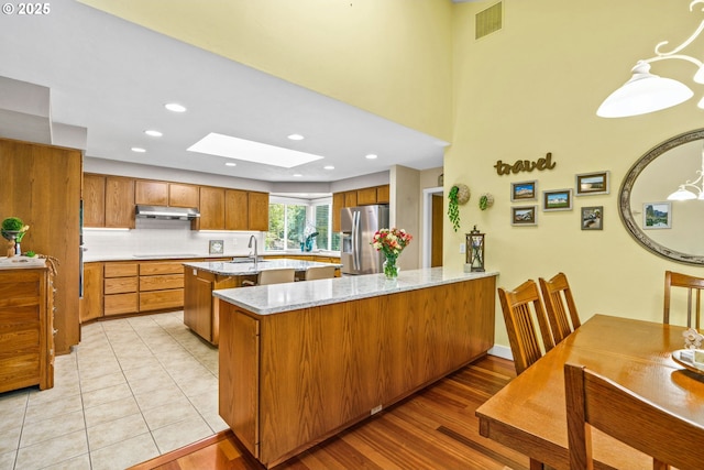 kitchen with stainless steel refrigerator with ice dispenser, visible vents, a skylight, brown cabinets, and a sink