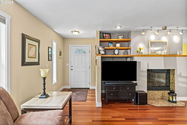 living room with baseboards, a glass covered fireplace, wood finished floors, and rail lighting