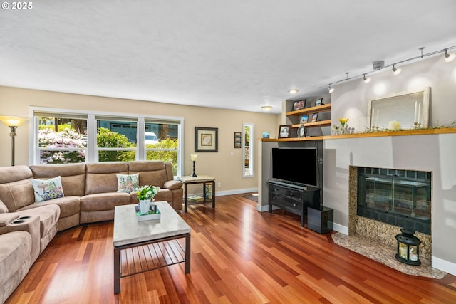 living room with a fireplace with flush hearth, baseboards, wood finished floors, and track lighting