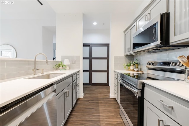 kitchen with gray cabinets, a sink, dark wood finished floors, appliances with stainless steel finishes, and light countertops