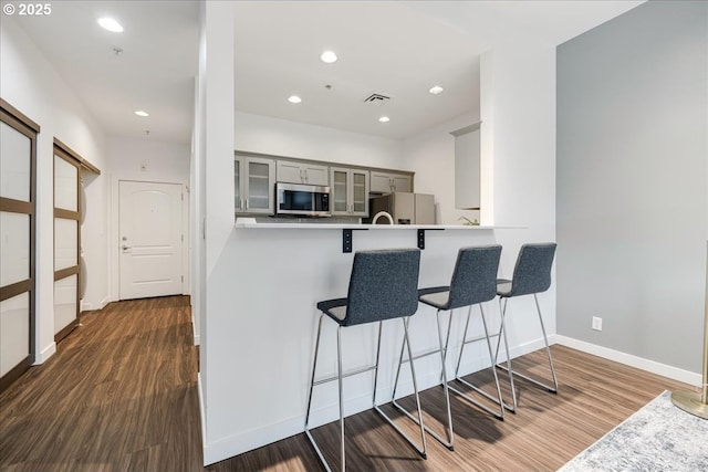 kitchen with gray cabinetry, stainless steel microwave, dark wood finished floors, white fridge with ice dispenser, and glass insert cabinets