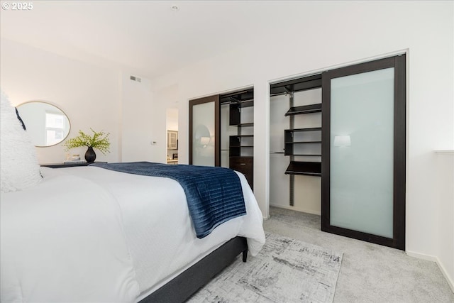 bedroom with two closets, baseboards, visible vents, and carpet floors