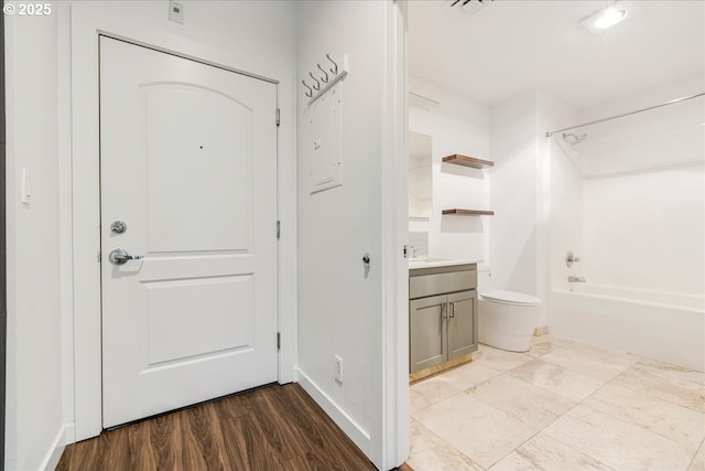 interior space with vanity, wood finished floors, baseboards, bathing tub / shower combination, and toilet