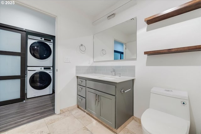 bathroom with tasteful backsplash, stacked washer / dryer, toilet, and vanity