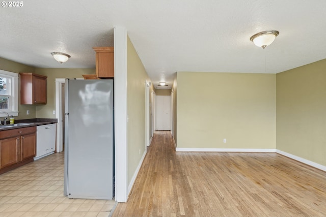 kitchen featuring stainless steel refrigerator, sink, white dishwasher, a textured ceiling, and light hardwood / wood-style flooring