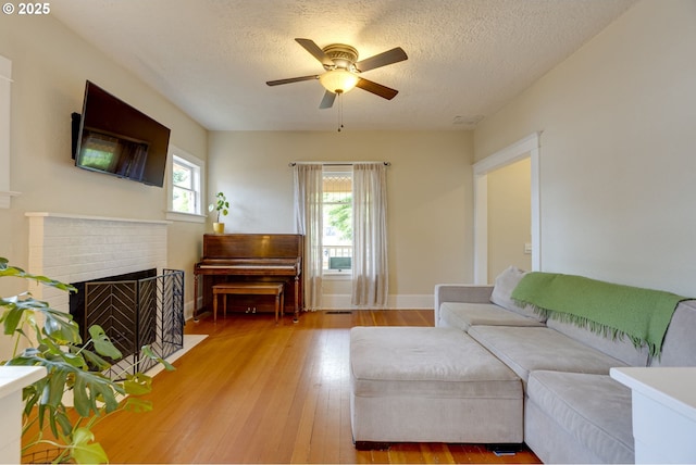 8113 SE Morrison St, Portland, OR 97215 - living room featuring ceiling fan, light wood finished floors, a brick fireplace, baseboards, and a textured ceiling