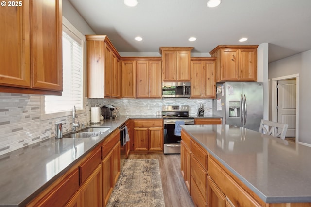 kitchen with stainless steel appliances, a sink, light wood finished floors, and tasteful backsplash