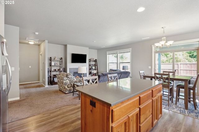 kitchen with a kitchen island, stainless steel refrigerator with ice dispenser, decorative light fixtures, light wood finished floors, and a chandelier
