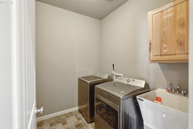 laundry room featuring washing machine and dryer, baseboards, stone finish flooring, a sink, and cabinet space