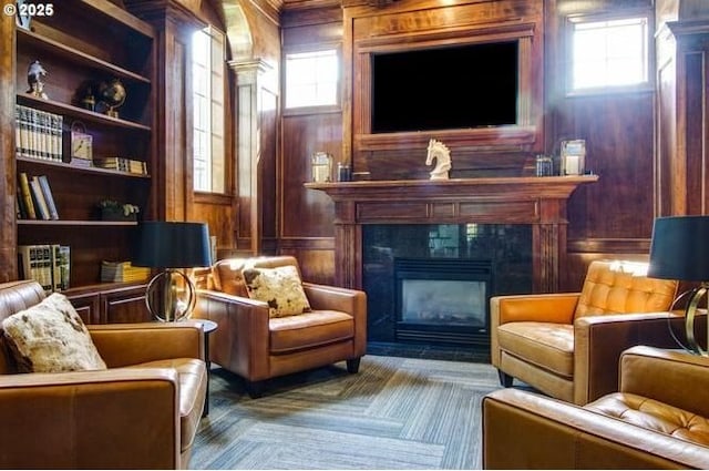 living area featuring decorative columns, built in shelves, wood walls, and a tile fireplace