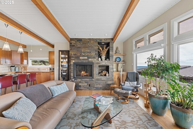 living room featuring beam ceiling, a stone fireplace, and light wood-type flooring