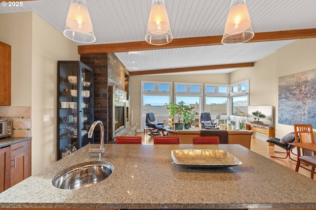 kitchen featuring sink, light stone counters, tasteful backsplash, a center island with sink, and decorative light fixtures