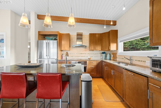 kitchen with sink, a breakfast bar, a kitchen island with sink, stainless steel appliances, and wall chimney exhaust hood