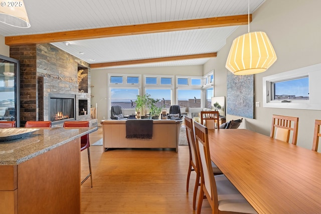 dining space with beamed ceiling, a stone fireplace, and light wood-type flooring