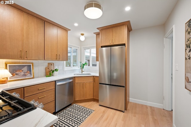 kitchen with tasteful backsplash, light countertops, light wood-style flooring, appliances with stainless steel finishes, and a sink