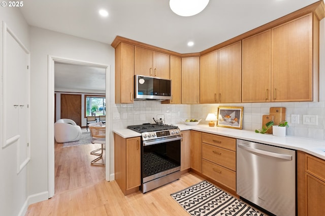 kitchen featuring light countertops, tasteful backsplash, light wood-type flooring, and appliances with stainless steel finishes