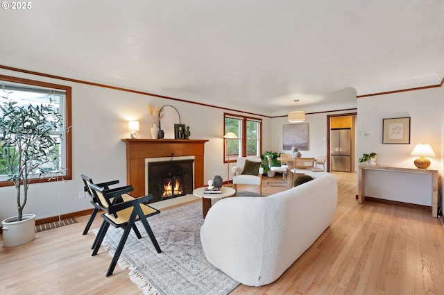 living area with crown molding, a fireplace with flush hearth, and light wood-type flooring