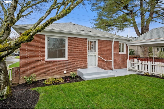 rear view of house with brick siding, a lawn, roof with shingles, and fence