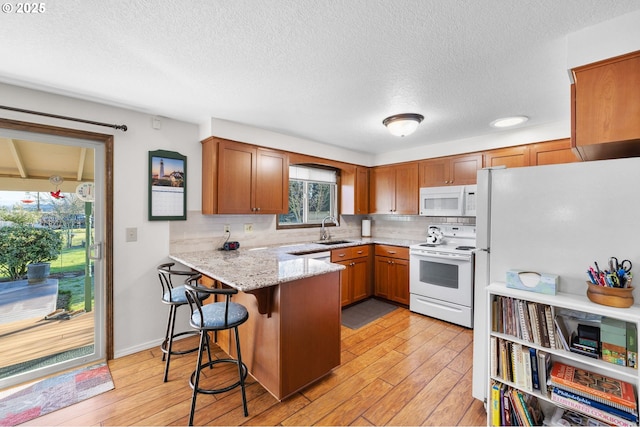 kitchen featuring sink, a breakfast bar area, light hardwood / wood-style floors, kitchen peninsula, and white appliances