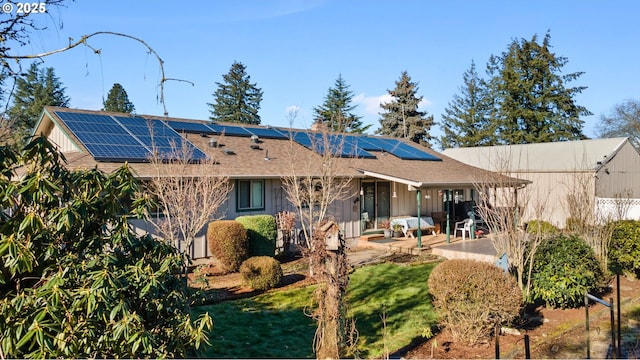 rear view of property featuring a lawn, a patio area, and solar panels