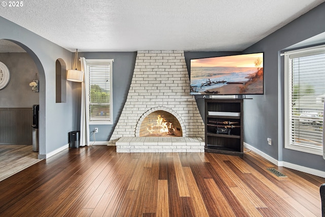 3780 SE 21st Dr, Gresham, OR 97080 - unfurnished living room featuring a brick fireplace, arched walkways, a textured ceiling, hardwood / wood-style flooring, and baseboards