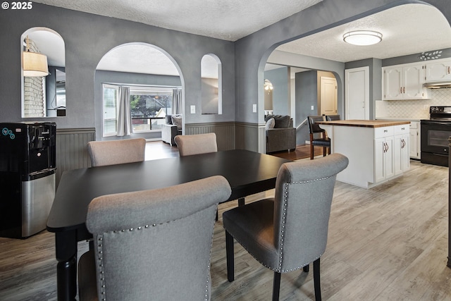 3780 SE 21st Dr, Gresham, OR 97080 - dining area featuring arched walkways, a textured ceiling, a wainscoted wall, and light wood-type flooring
