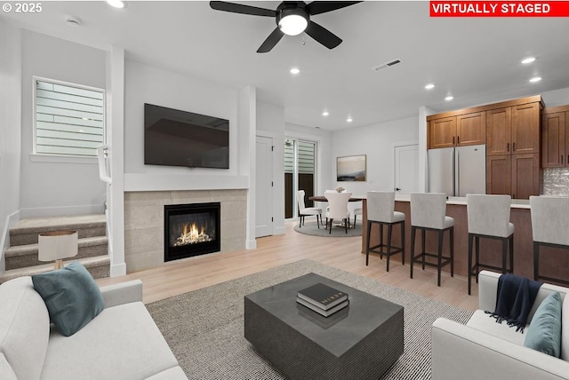 living room featuring a fireplace, ceiling fan, and light wood-type flooring